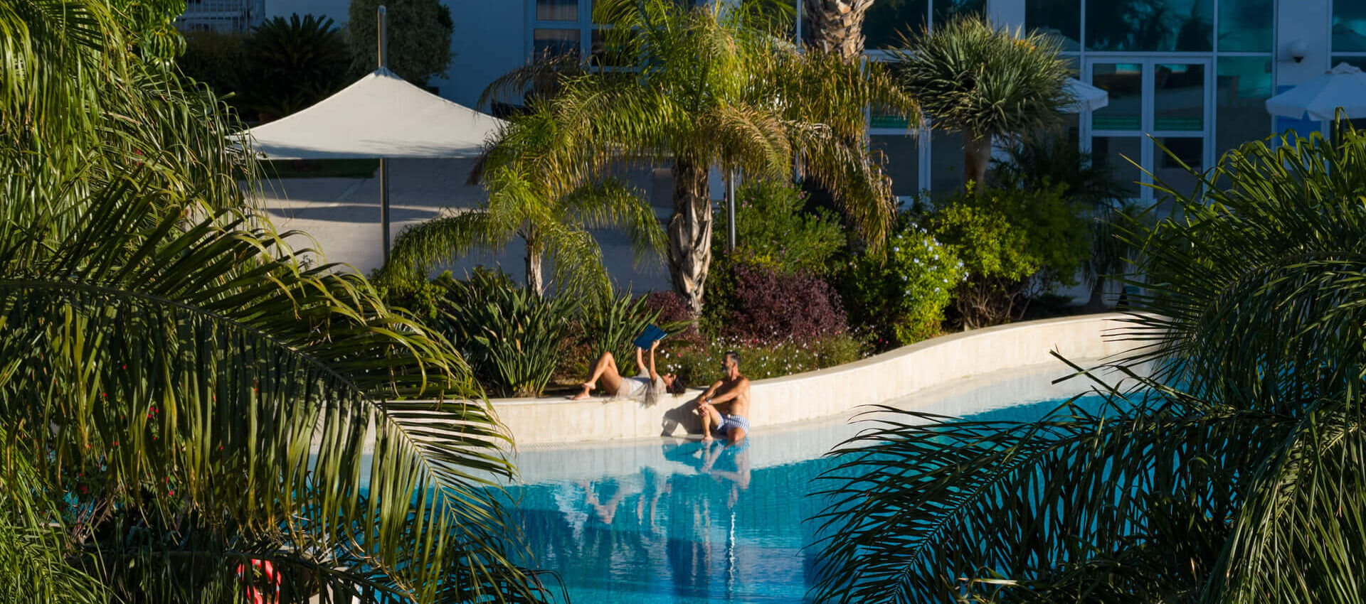 Couple relaxing at pool at Hilton Nicosia surrounded by palm trees