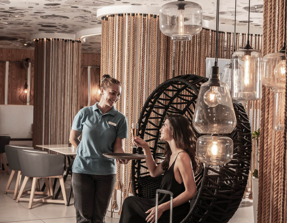 Woman with luggage getting a drink at King Jason Protaras Lounge area