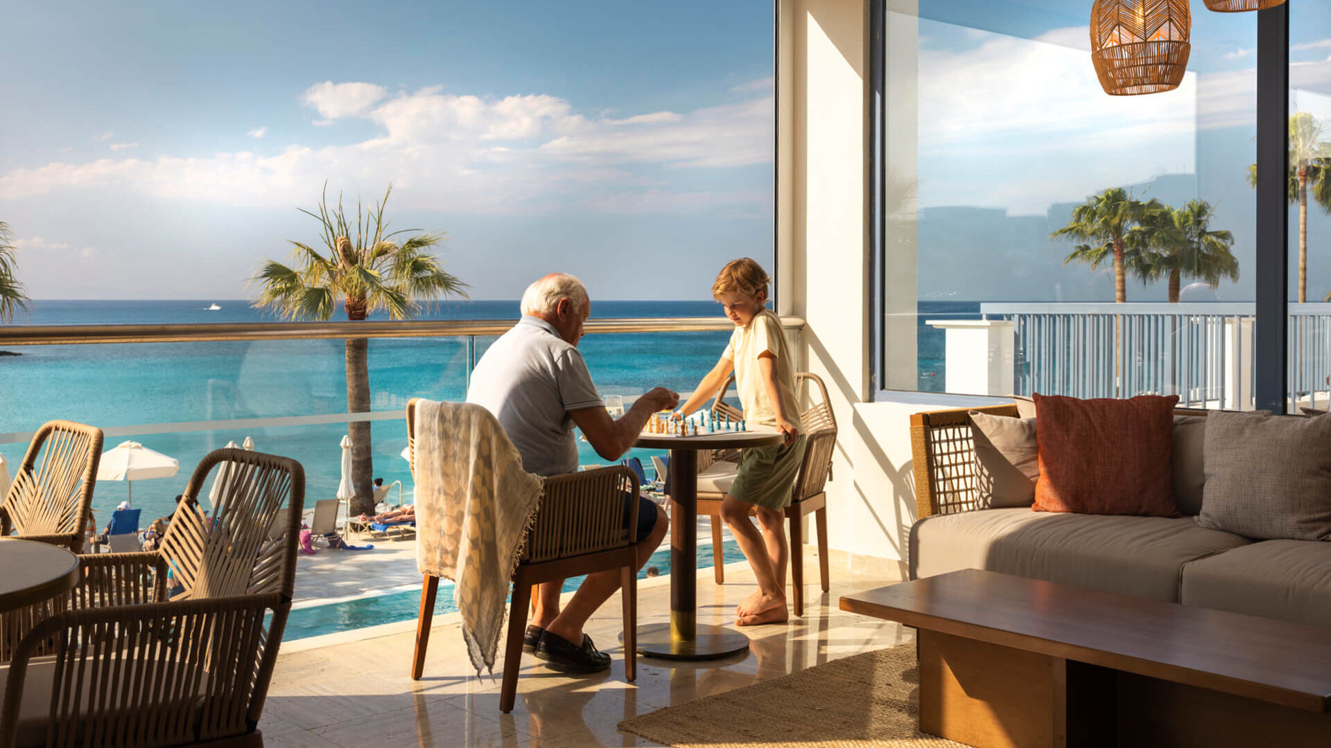 Grandparent and child playing chess at Louis Nausicaa Beach bar table with sea view