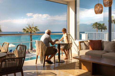 Grandparent and child playing chess at Louis Nausicaa Beach bar table with sea view