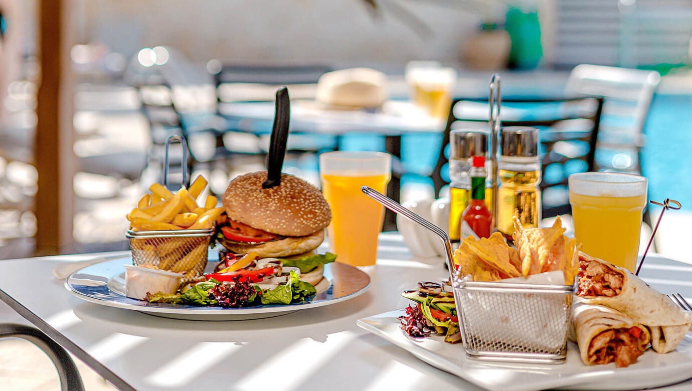 Table with burger and burrito poolside at Louis Althea restaurant