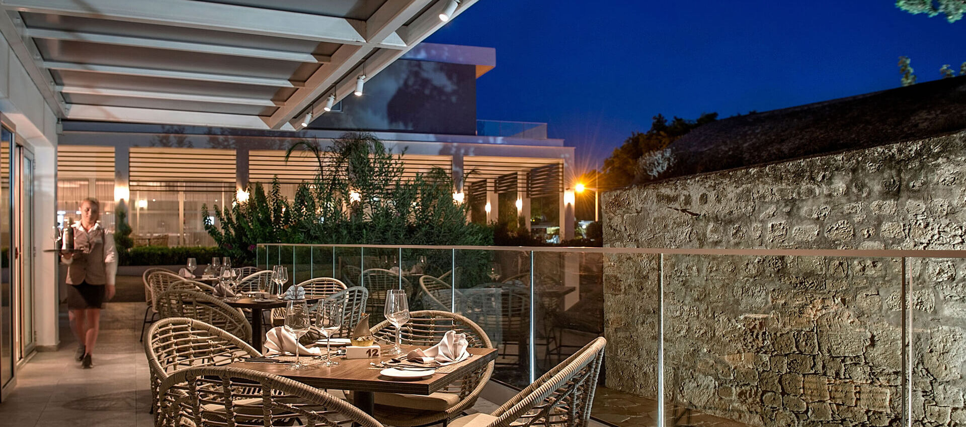 Waiter walking with wine next to tables at Sofianna Resort restaurant