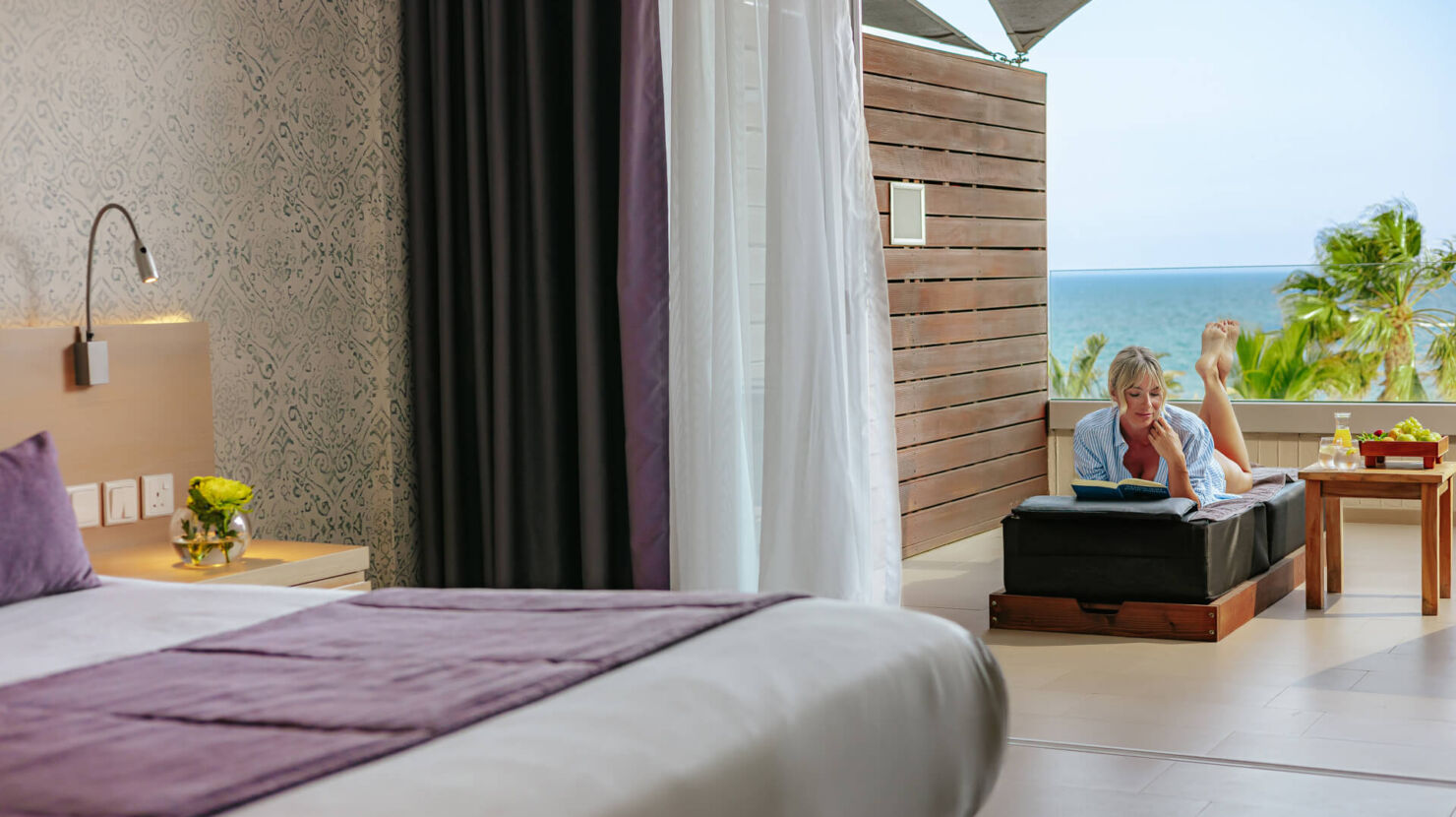 Royal Apollonia Deluxe room bedroom and balcony with woman sitting at chair