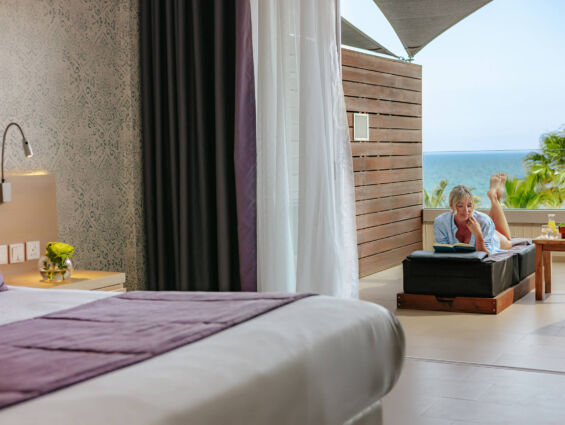 Royal Apollonia Deluxe room bedroom and balcony with woman sitting at chair