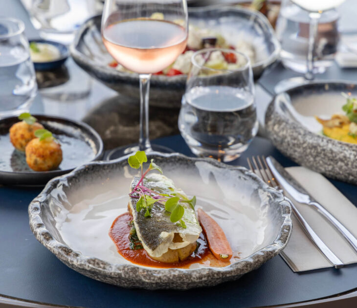 Table with main dishes and wine with sea view at Valmar Corfu Gill Restaurant